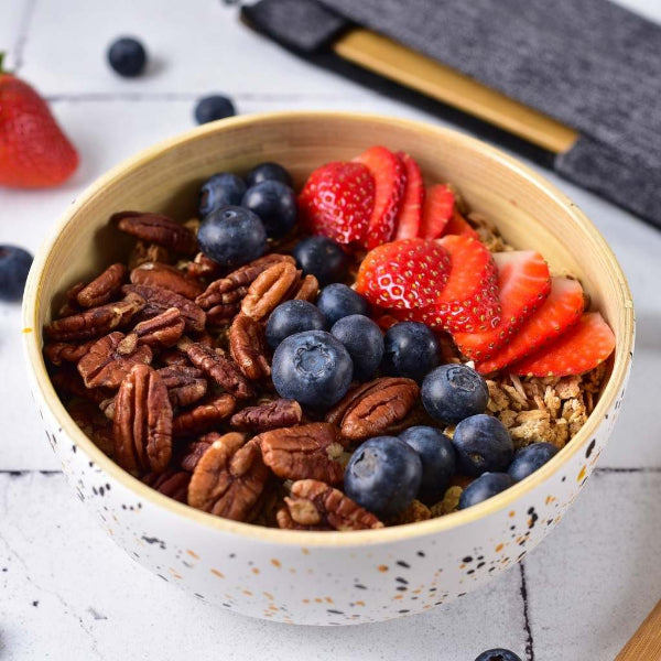 Bamboo white painted bowl of granola with berries and nuts on a light surface