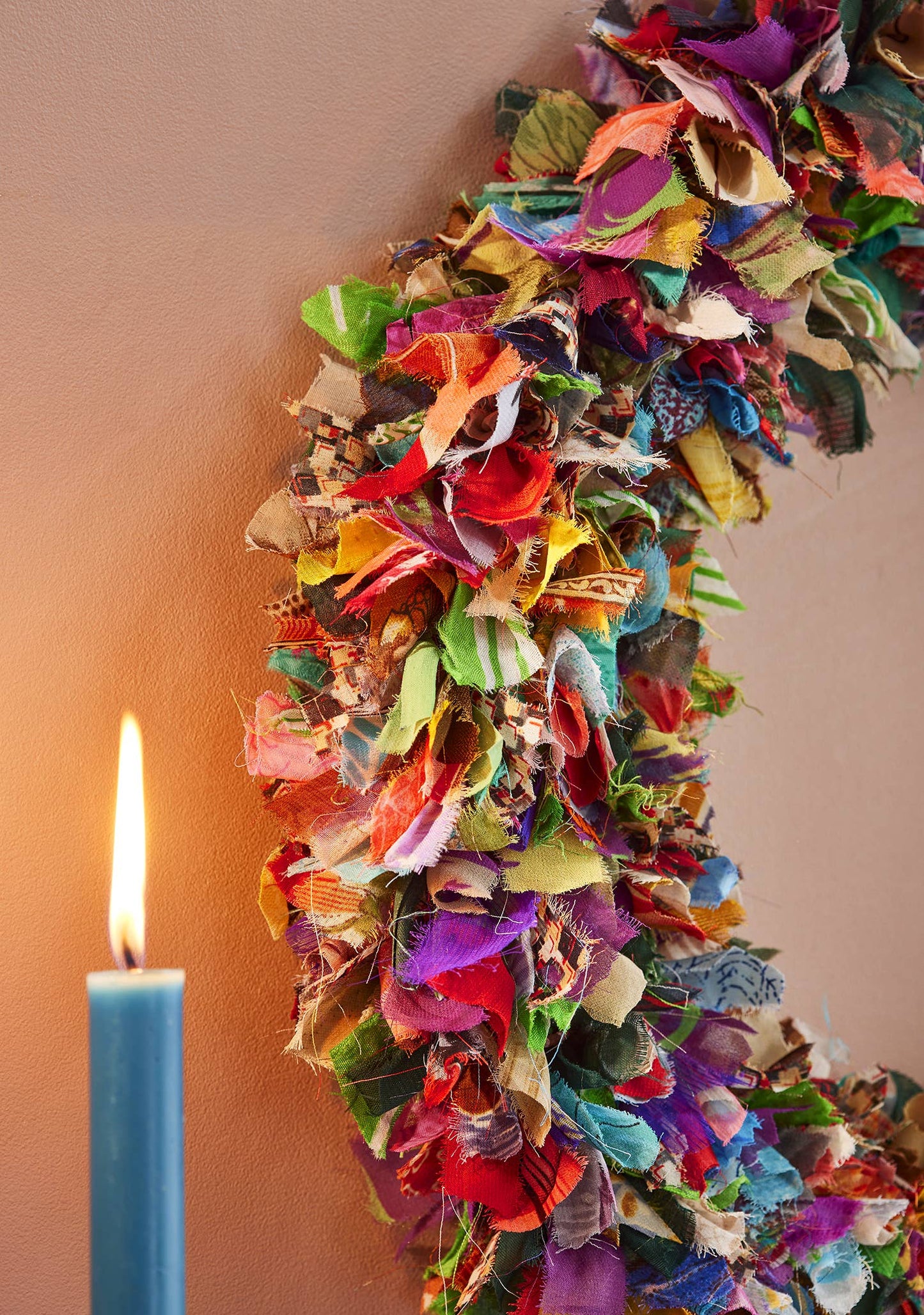 Colorful recycled sari fabric wreath with a lit candle on a plain background