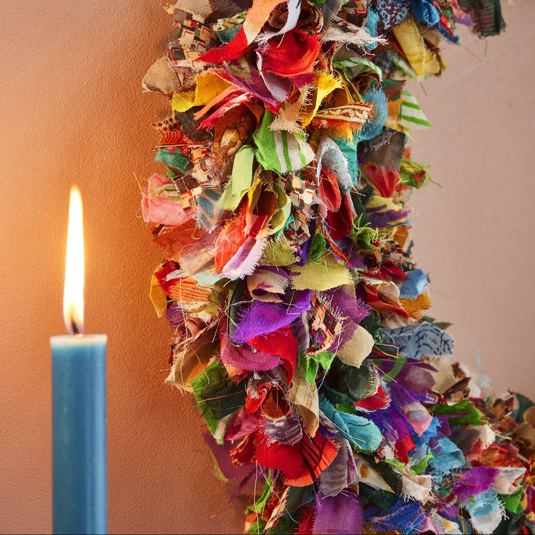 Colorful recycled sari fabric wreath with a lit candle on a plain background