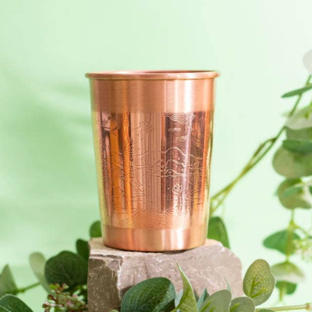 Copper cup on a stone block with green leaves and flowers on a light green background