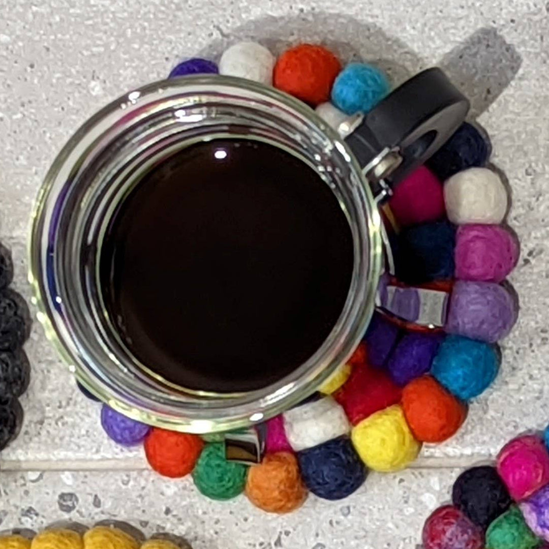 Colorful felt coasters on a textured surface with a cup of coffee.