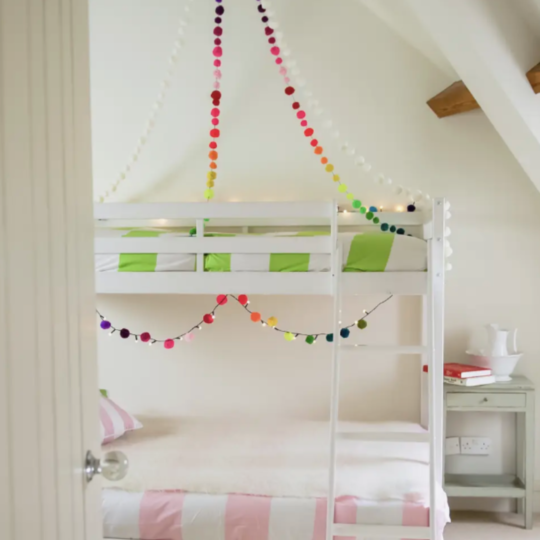 White bunkbed decorated with rainbow pompom light chain