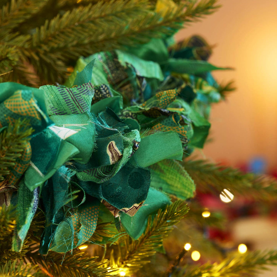 A close-up of a green fabric garland with patterned ruffles, hanging on a Christmas tree