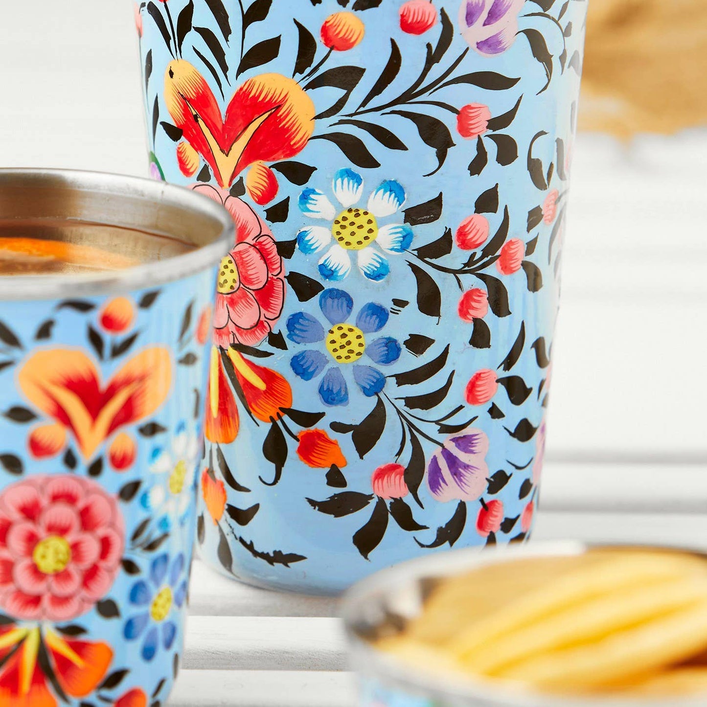 hand painted enamel large tumbler light blue background black leaves and stems, red-pink-blue-yellow flowers