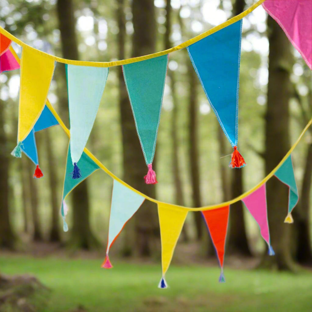 rainbow coloured bunting draped between trees on a woodland campsite.