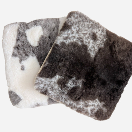 Two sheepskin seat pads, one dark brown with light brown patches; the other mostly cream with light brown patches.