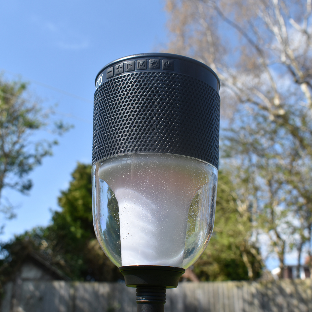 colour change lantern and speaker with ground spike pictured with garden background, grey fence, trees
