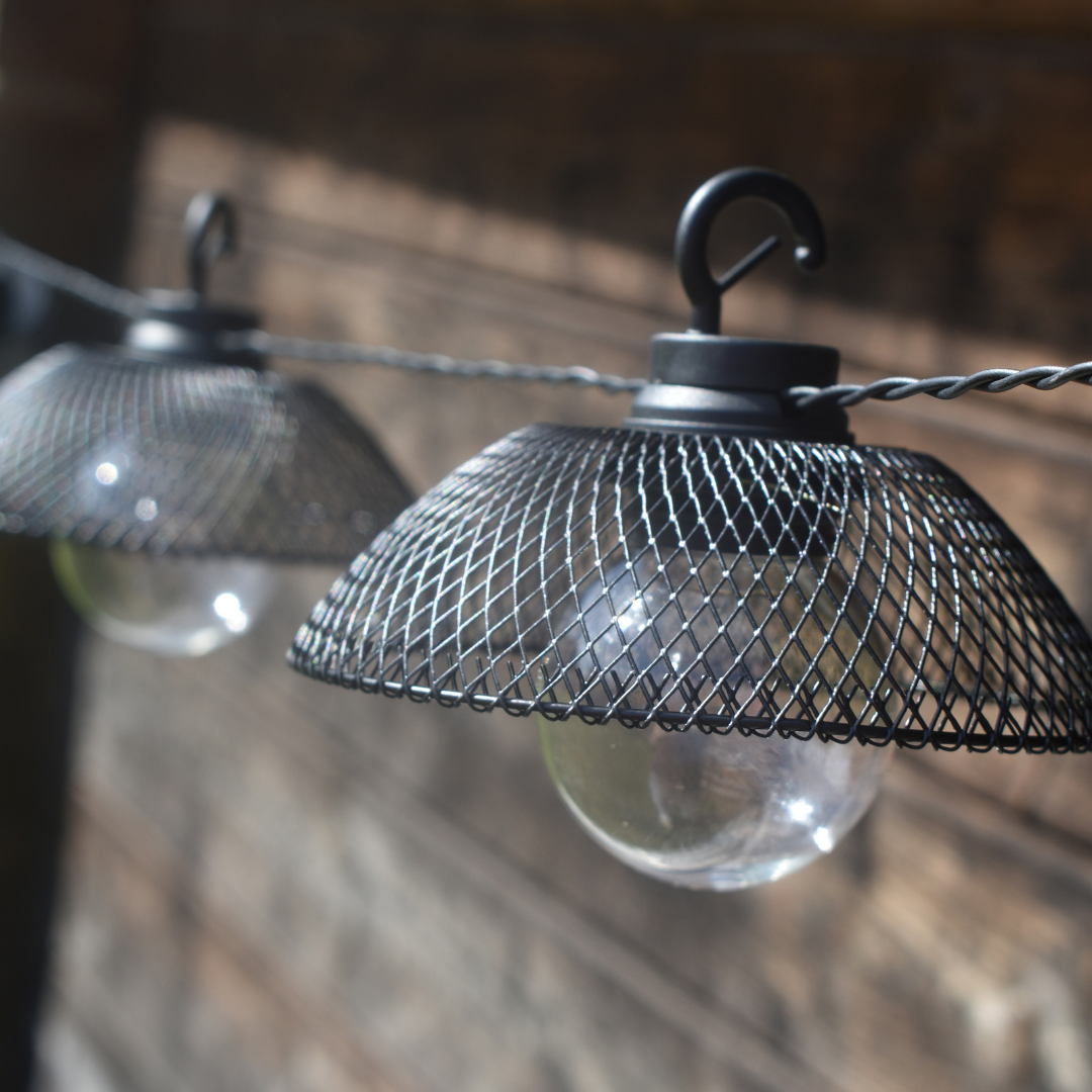 Close up of two of the 10 black mesh lanterns with round bulbs, garden shed background.