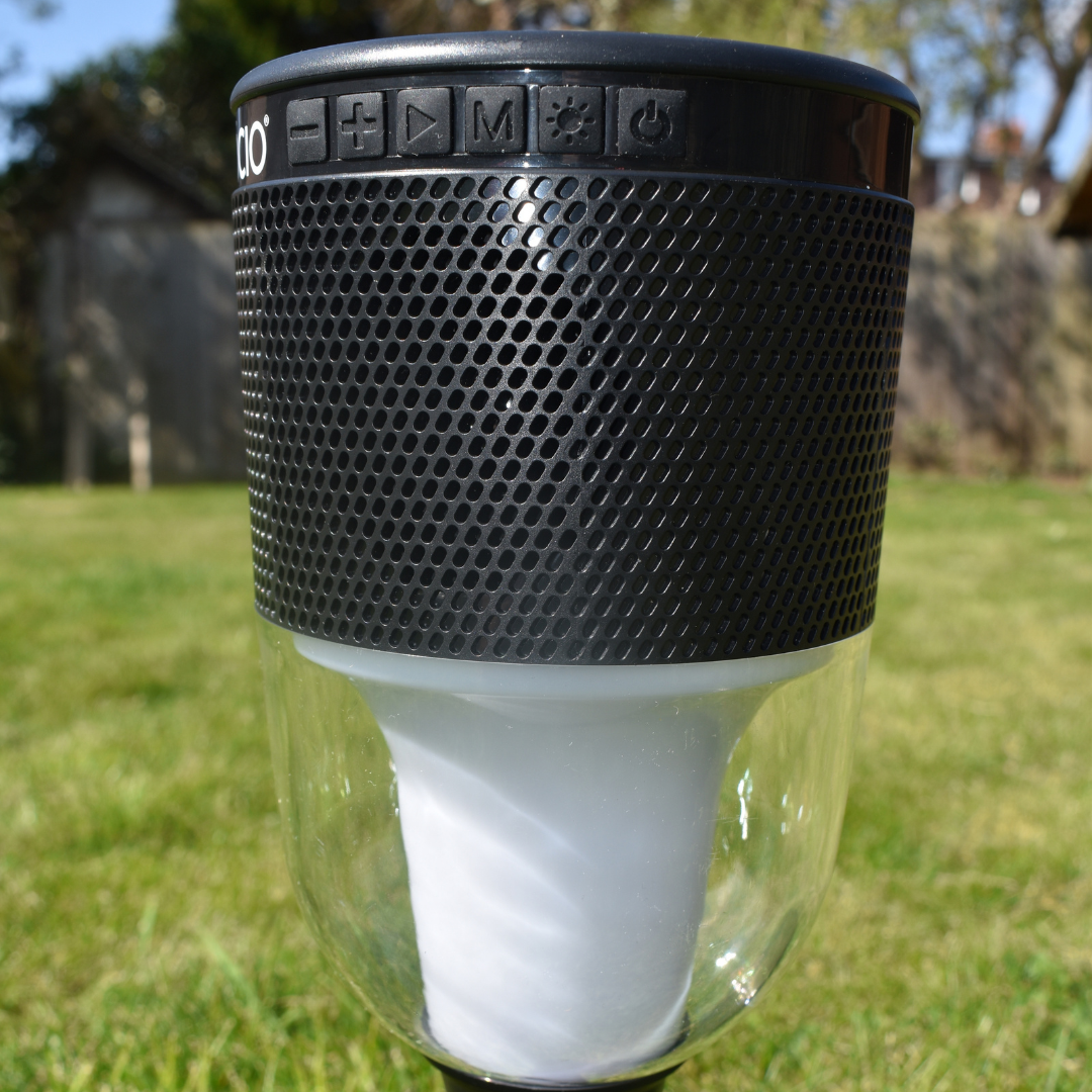 close up colour change lantern and speaker with ground spike pictured green grass background, black solar panel on top and speaker control.