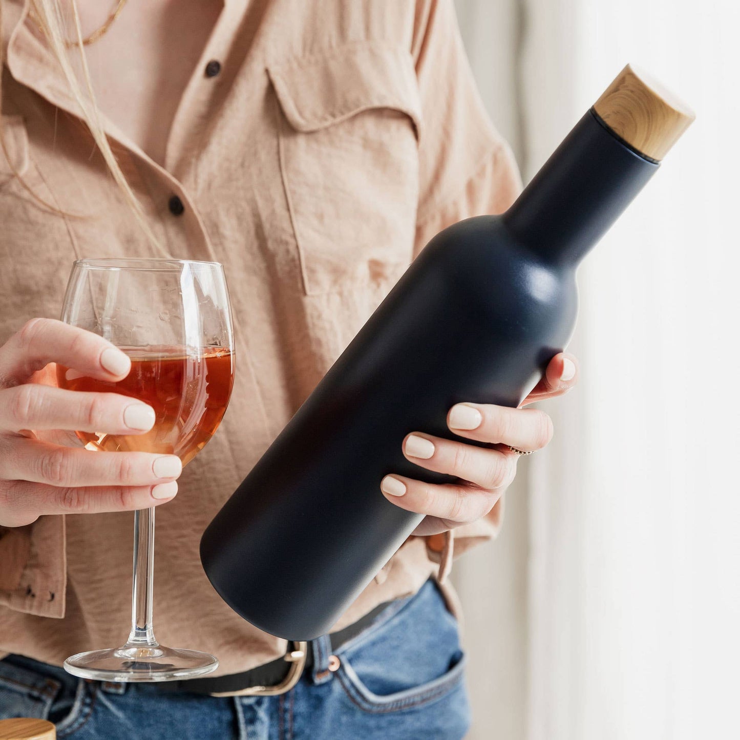 female holding glass of pink wine and navy insulated travel wine bottle