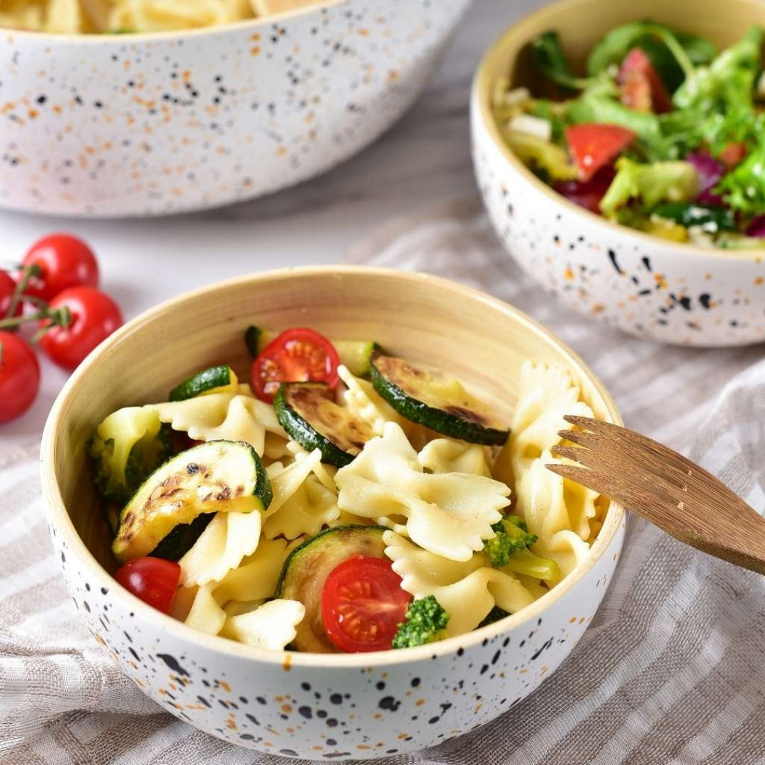 Bamboo bowls of pasta with vegetables on a textured surface