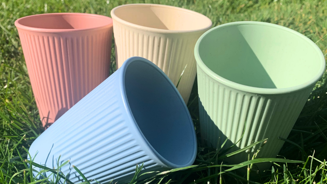 four multi-coloured cups made from wheat straw plastic, on a grassy background.