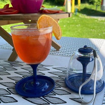 Two clear plastic wine glasses with royal blue stem and wide base. Left glass filled with aperol spritz with orange slice. Right glass packed away with carry lanyard.