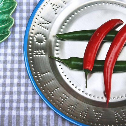 Metallic plate with blue trim and engraved text "Bon Appetit" on a blue gingham background