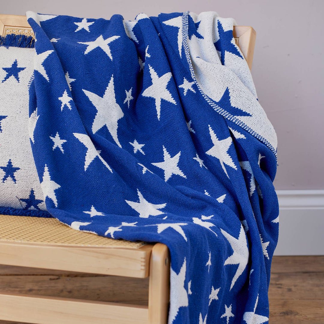 A blue and white star-patterned throw blanket draped over a wooden bench, with matching star-printed cushion.
