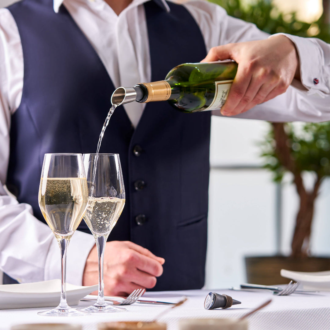 sparkling wine being poured from a stainless steel chill stick and wine bottle.