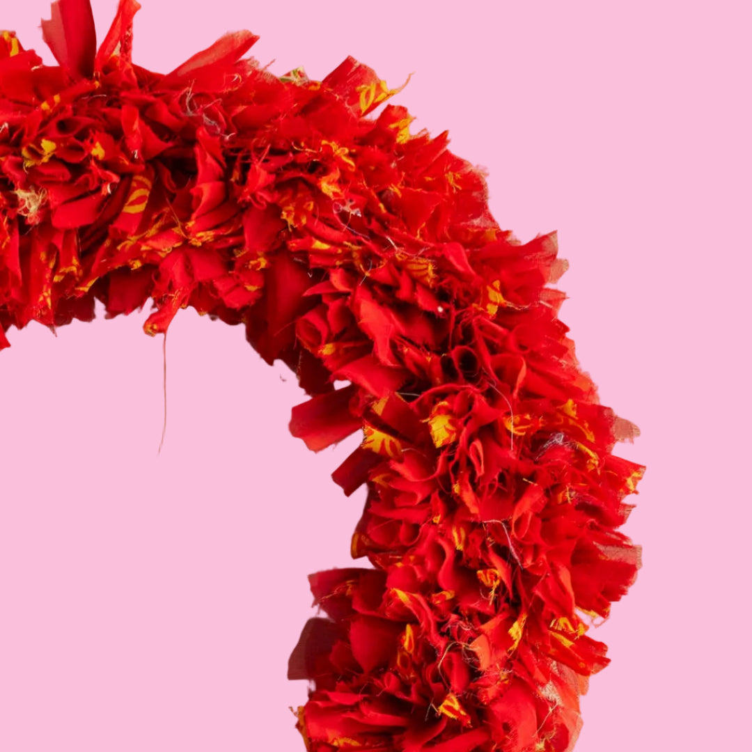 A close up of a red fabric wreath with a quarter of the large circle pictured on a pink background.