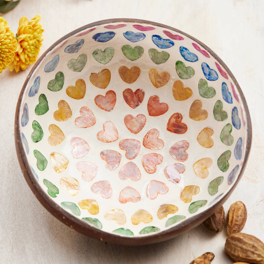 Decorative coconut shell bowl with multicoloured heart pattern on a light background.