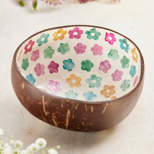 coconut bowl with floral pattern inside, surrounded by flowers on a light background