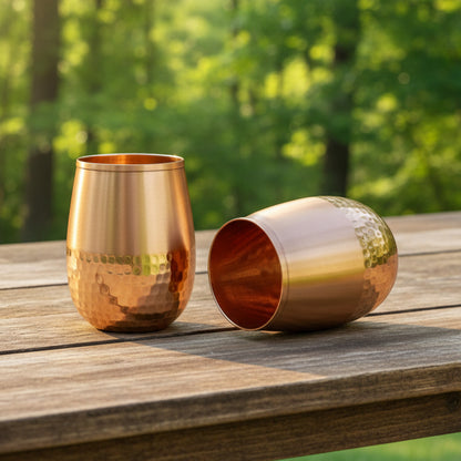 Two hammered copper cups on a wooden table one standing upright and the other lying on its side