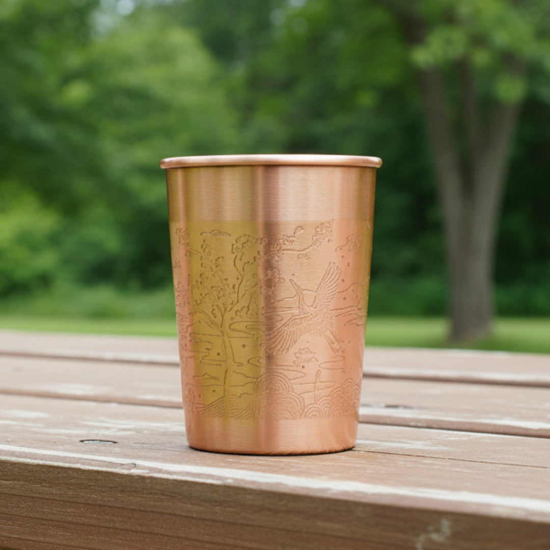 Copper tumbler with embossed design on an outdoor background.