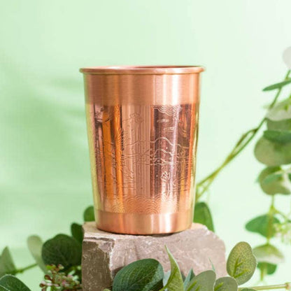 Copper cup on a stone block with green leaves and flowers on a light green background