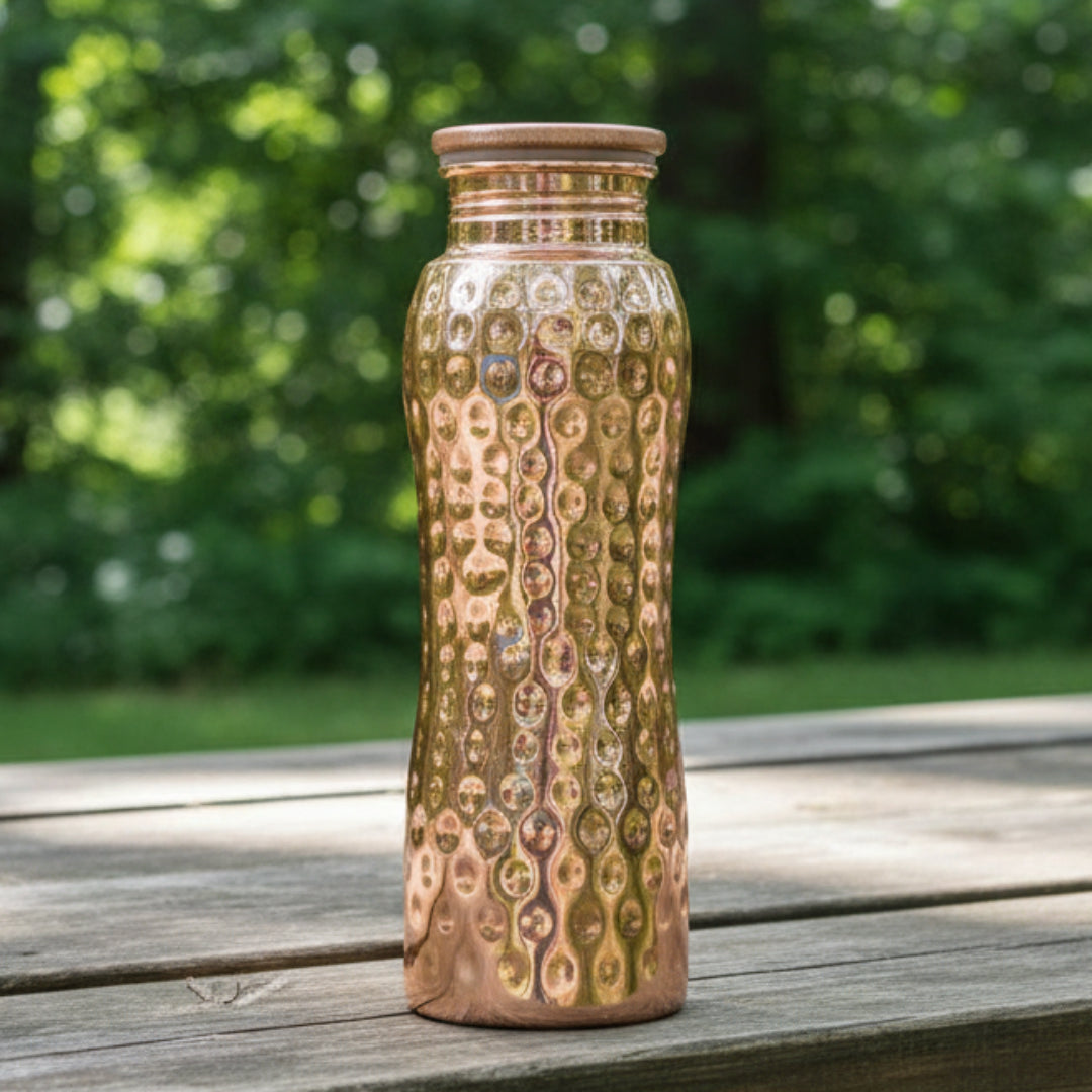 Copper water bottle with a textured surface on a picnic bench on a blurred green background