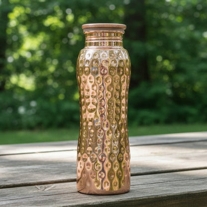 Copper water bottle with a textured surface on a picnic bench on a blurred green background
