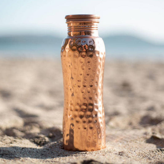Copper water bottle on a sandy beach with a blurred background