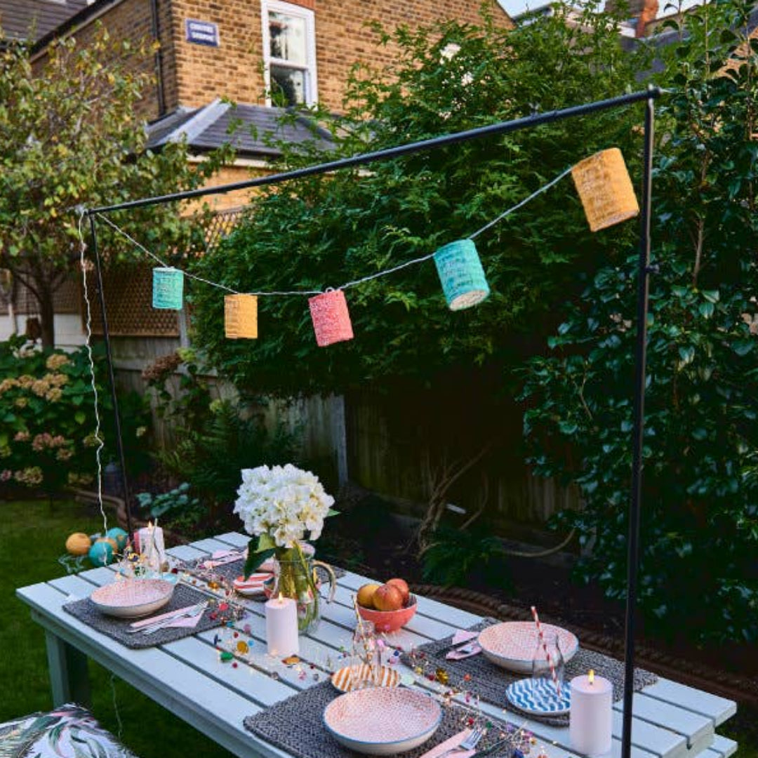Outdoor dining setup with a table, chairs, and decorative solar lanterns in a garden.