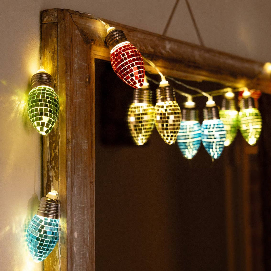 String lights with colorful disco ball bulbs hanging against a wooden frame.