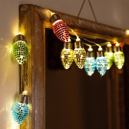 String lights with colorful disco ball bulbs hanging against a wooden frame.