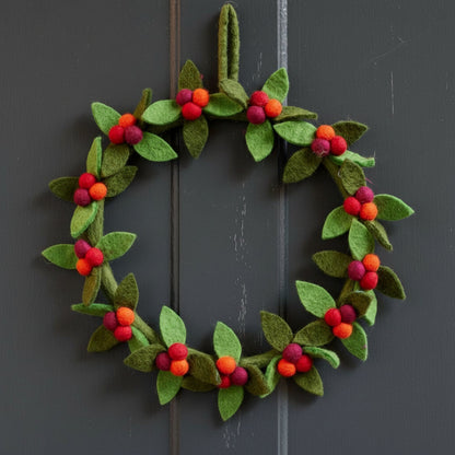 Decorative felt wreath with green leaves and red berries hanging on a grey front door