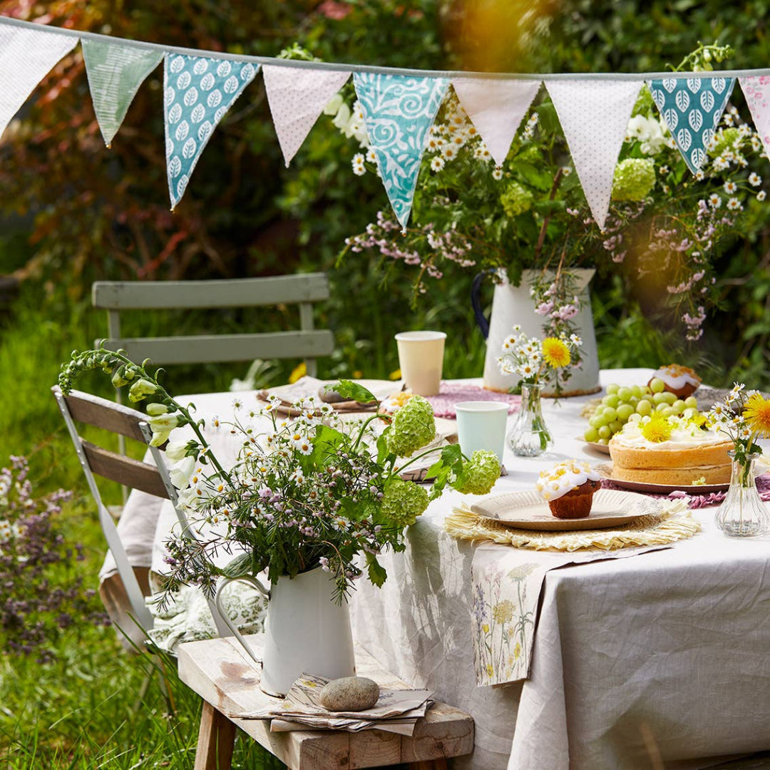 Outdoor table setting with flowers, fruits, and a bunting in a garden.