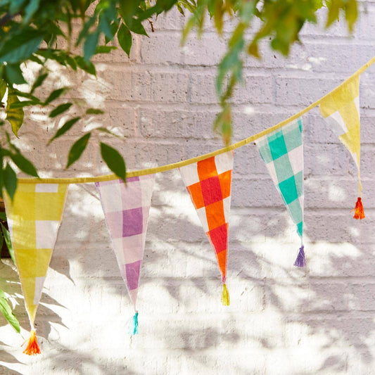 Colorful checkered bunting flags hanging against a light gray brick wall.