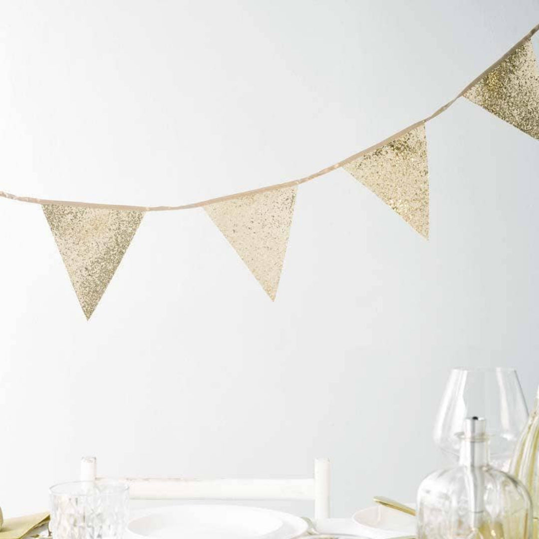 Gold glitter bunting across a table with glasses and bottles on a white background