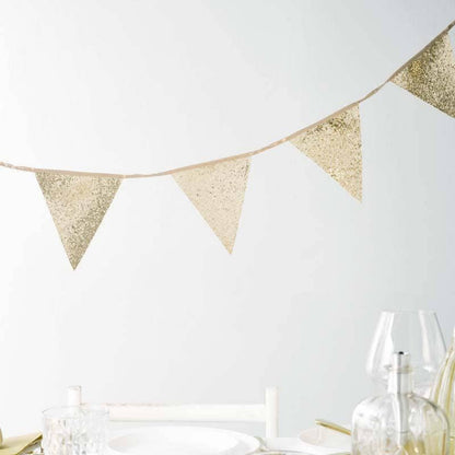 Gold glitter bunting across a table with glasses and bottles on a white background