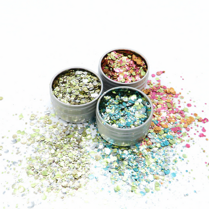 Three small containers filled with colorful glitter on a white background