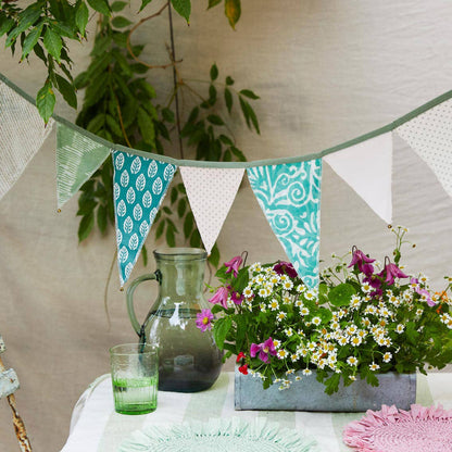 Decorative bunting with patterned flags, flowers, and a pitcher on a table.