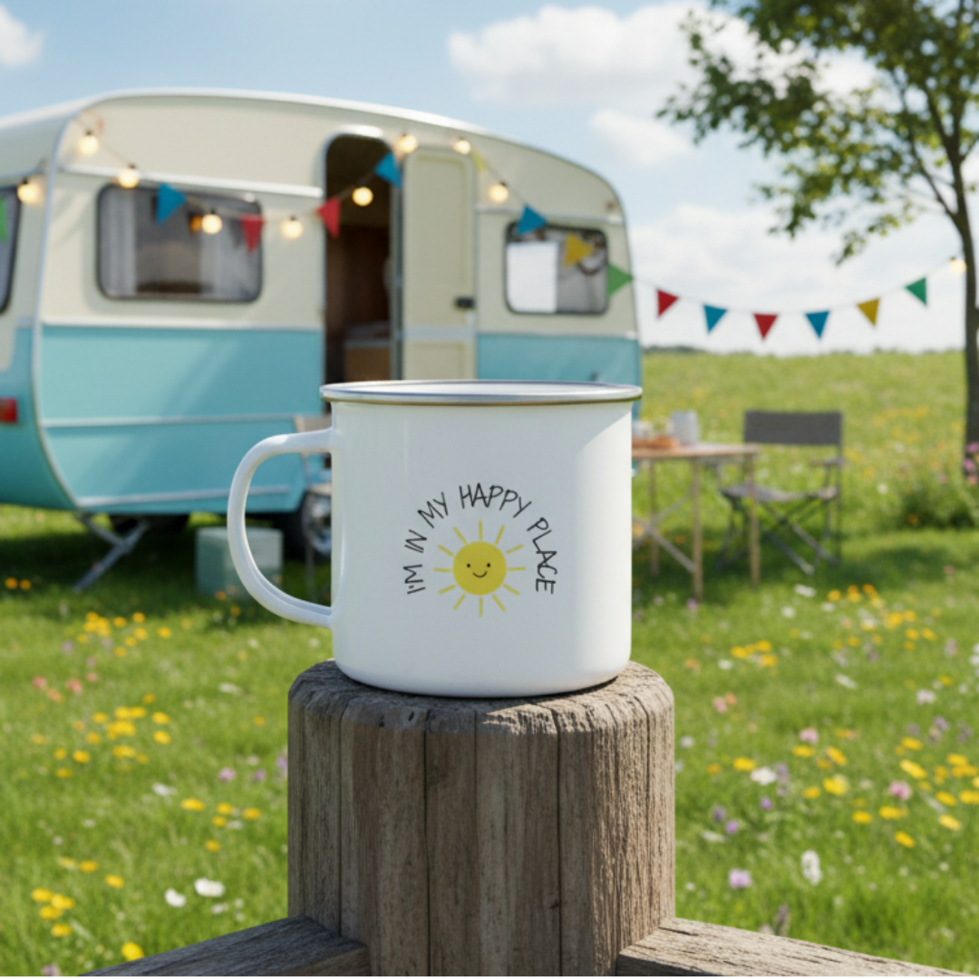 A white enamel mug with a handle, featuring a graphic of a sun and text that reads 'I'M IN MY HAPPY PLACE'.