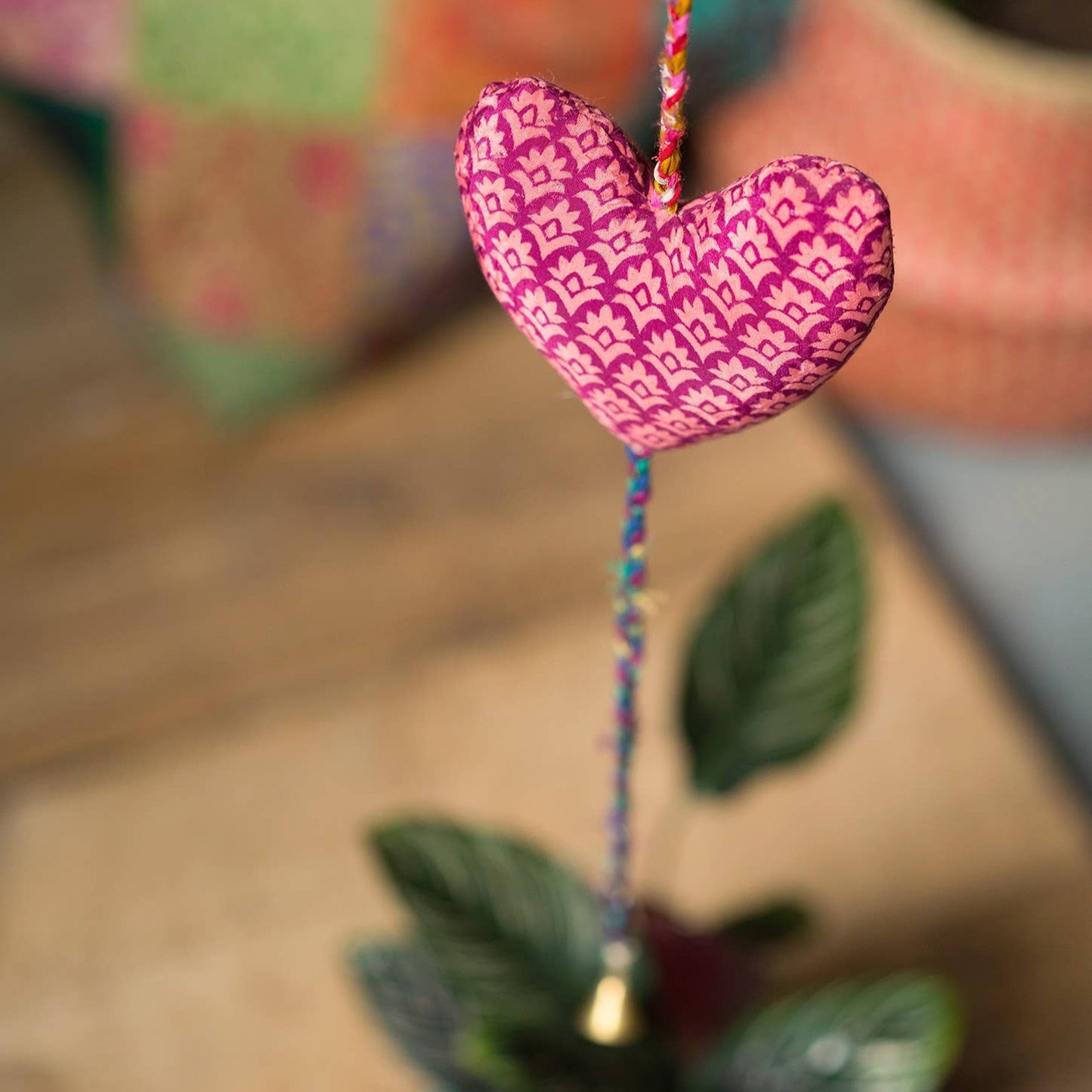 Bottom heart from decorateive heart string of three made from recycled sari material. This heart is dark pink with a lighter pink flower detail. There is a small bell at the end of the string.