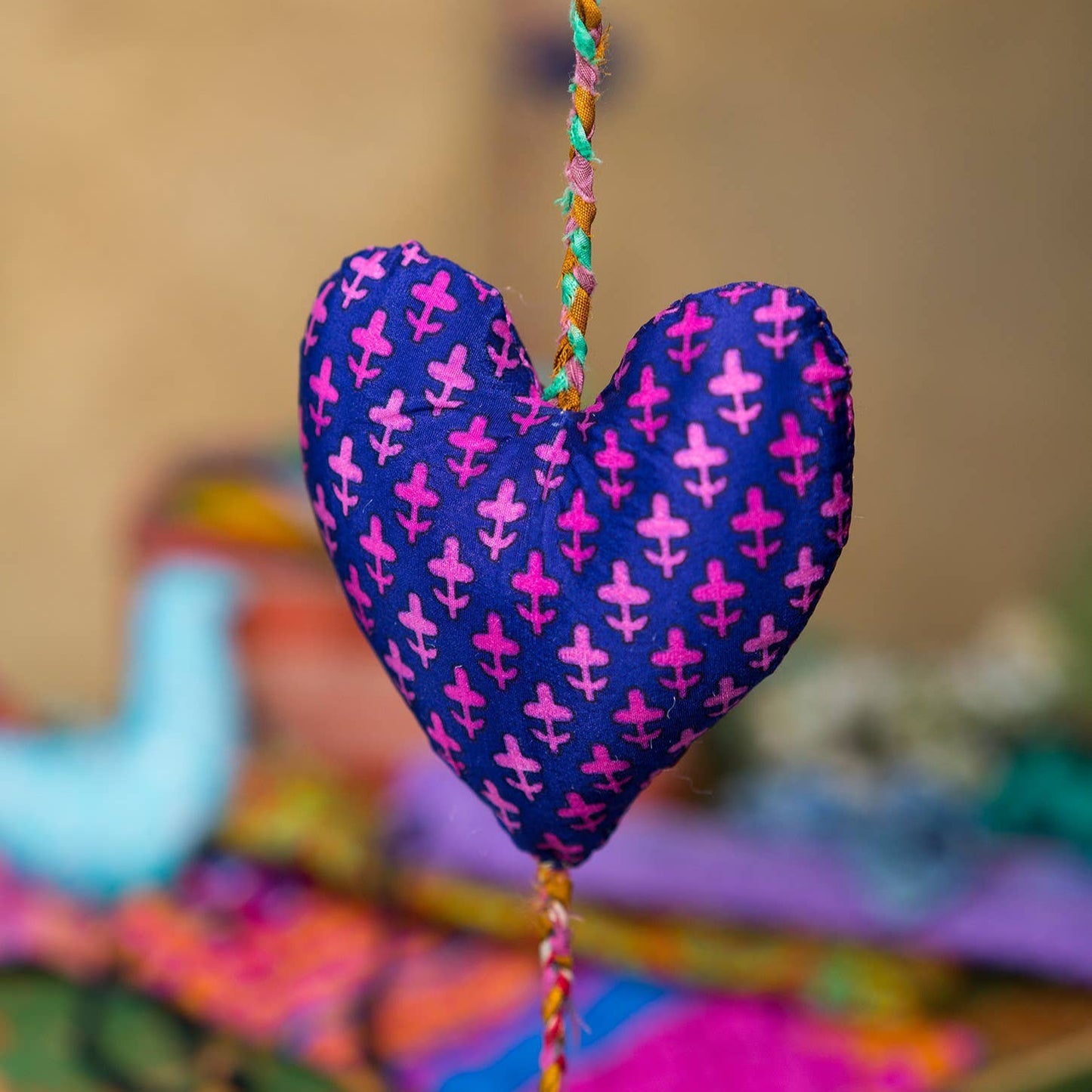 central heart of decorative string of three made from assorted recycled sari material. This heart is purple with pink flower detail.