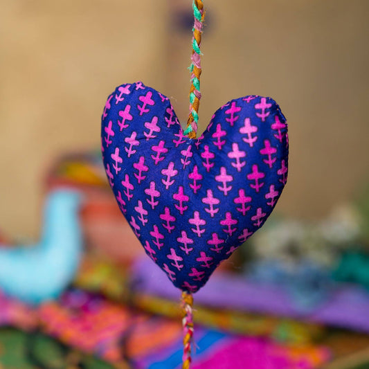 central heart of decorative string of three made from assorted recycled sari material. This heart is purple with pink flower detail.