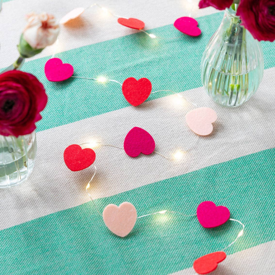 String of heart-shaped lights on a tablecloth with flowers and vases.