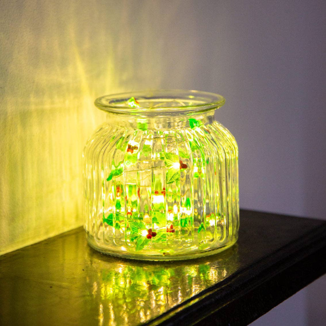 Glass jar with holly shaped LED lights inside on a reflective surface