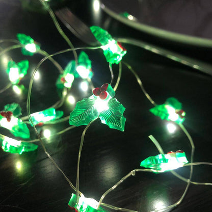 String lights with green holly-shaped bulbs with red berries on a dark background