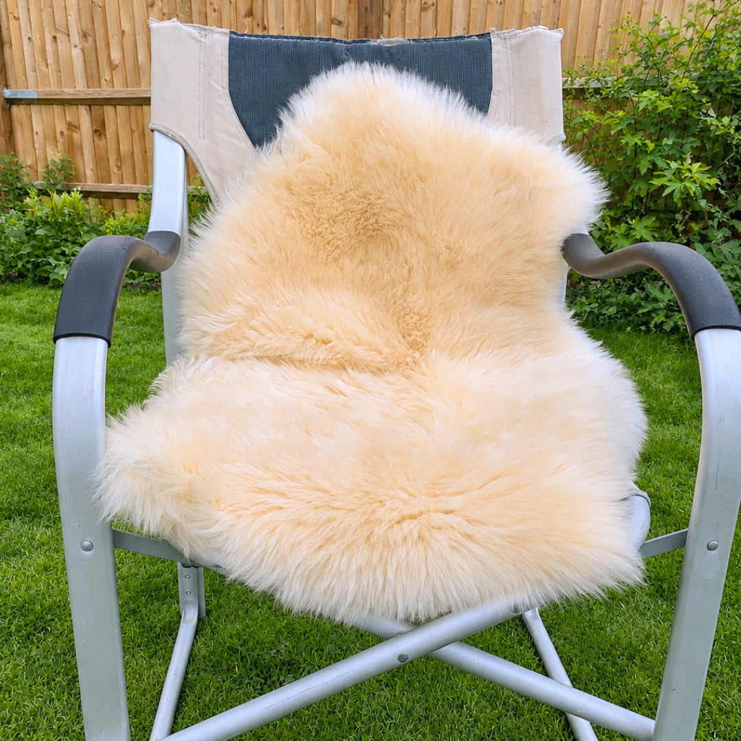A natural sheepskin draped over a metal folding outdoor chair in a backyard setting with a wooden fence and grass visible.
