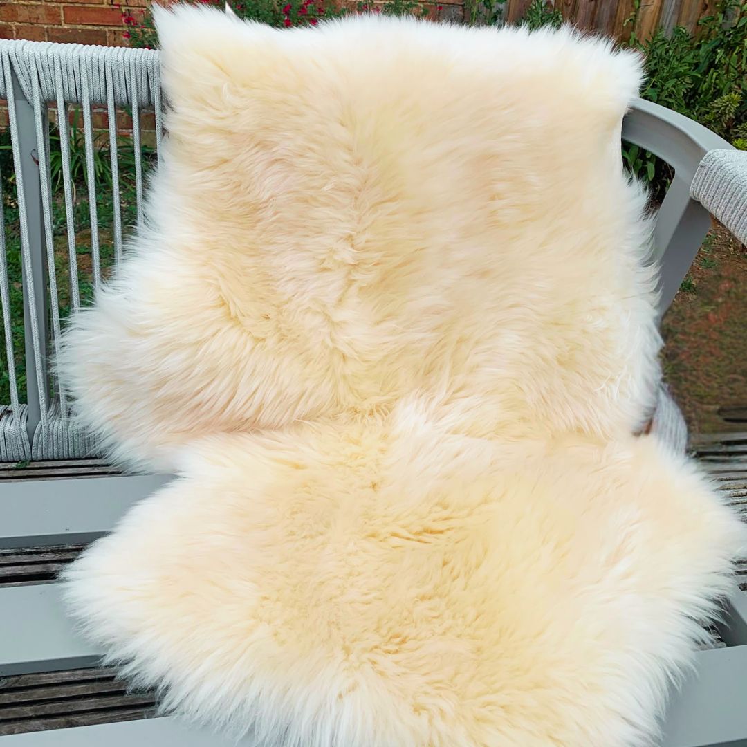 A natural coloured sheepskindraped over a grey outdoor patio chair, with a garden background visible.