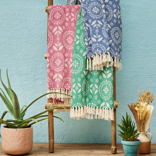 Colorful patterned throws in red, green and blue, hanging on a wooden ladder against a blue wall.