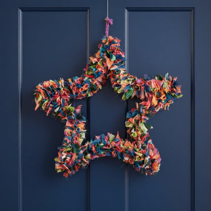 A star-shaped wreath made from colorful sari offcuts suspended against a blue door